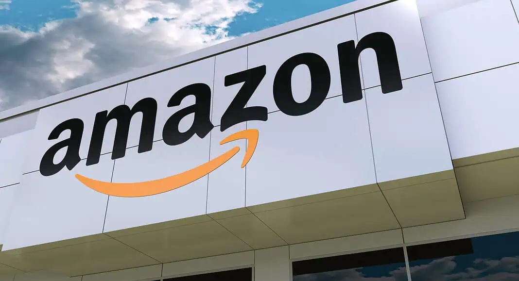 La facciata dell'edificio Amazon, impreziosita dal suo iconico logo con caratteri neri e una freccia gialla, si erge imponente sotto un cielo nuvoloso, incarnando l'essenza dell'automazione aziendale.