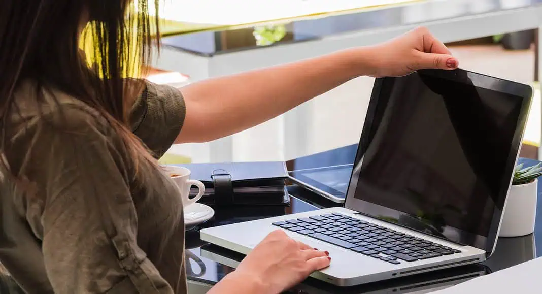Una persona apre un computer portatile sulla scrivania, attenta alla sicurezza della propria password, con un quaderno e una tazza di caffè nelle vicinanze, e si gode la quiete del mattino prima di dirigersi a una riunione al Comune di Bologna.