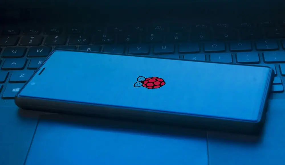 Uno smartphone è appoggiato sulla tastiera di un computer portatile e sullo schermo è ben visibile l'iconico logo rosso del Raspberry Pi.