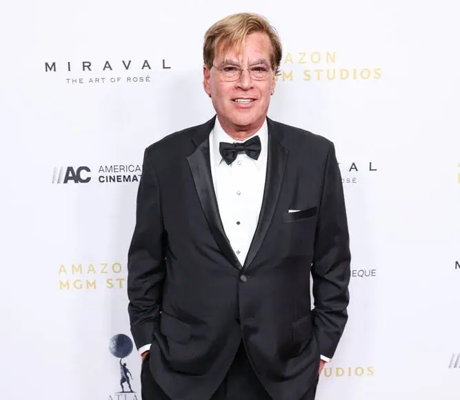 Un uomo in smoking si trova su un tappeto rosso davanti a un fondale bianco a gradini e ripetizioni, che ricorda la prima di The Social Network.