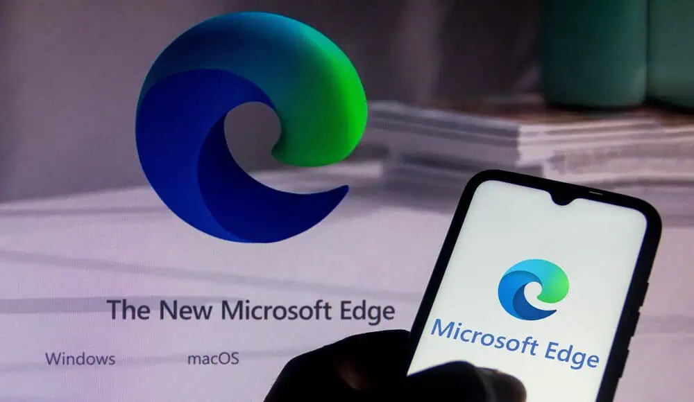 Una mano regge un telefono con il logo Microsoft Edge, visibile anche su uno schermo sullo sfondo.