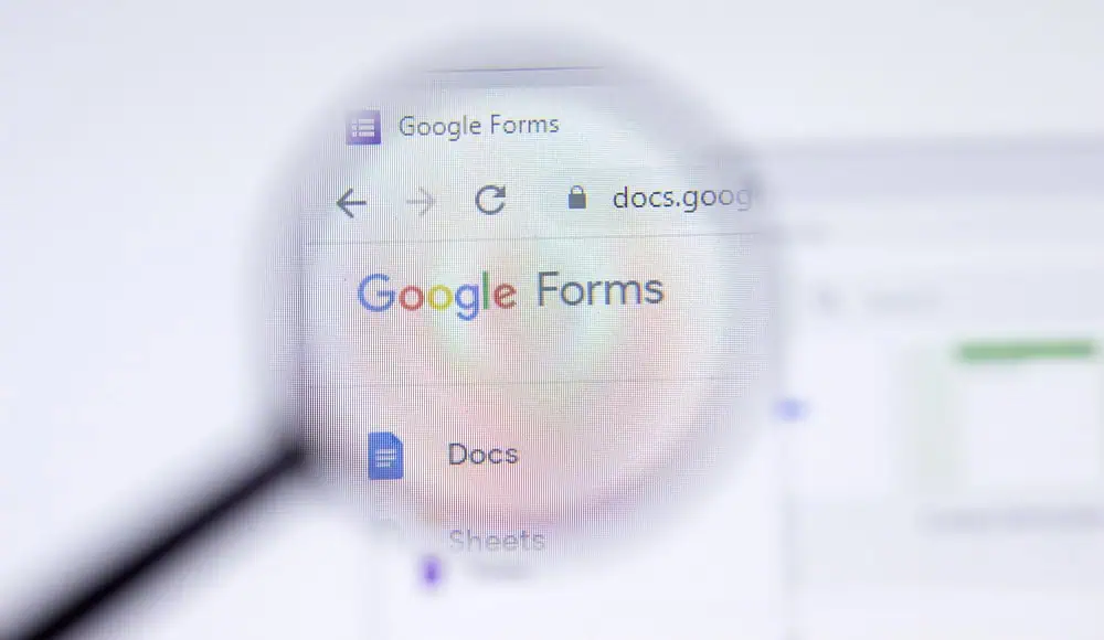 Una lente di ingrandimento si concentra sul logo della pagina web di Google Forms e sulla barra degli indirizzi di Google sullo schermo di un computer.