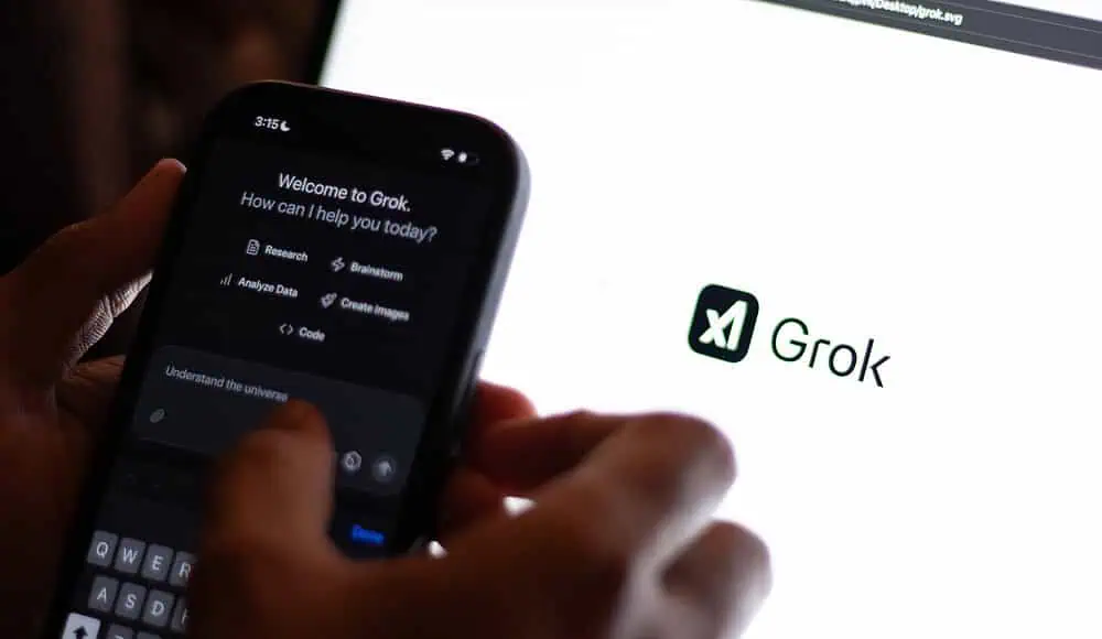 Una persona utilizza Grok 4 Fast AI su uno smartphone, con il logo Grok visualizzato sullo schermo di un computer portatile sullo sfondo.