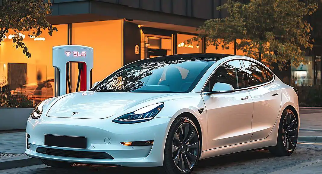 Un'elegante berlina Tesla bianca si ricarica presso una stazione Tesla Supercharger all'esterno di un edificio moderno.