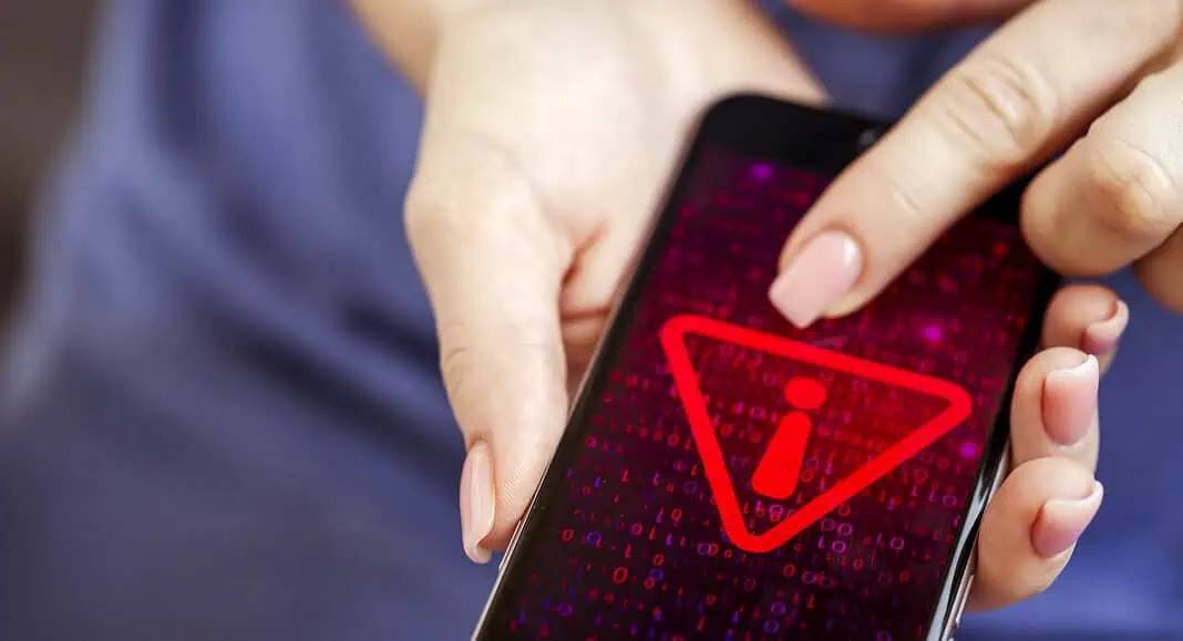 Una persona tiene in mano un Samsung Galaxy che mostra un simbolo di avvertimento rosso con un'icona informativa, invitando gli utenti ad aggiornare subito per non compromettere il telefono.