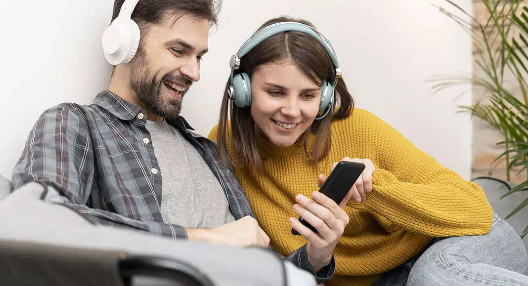 Due persone con le cuffie che sorridono e guardano insieme uno smartphone Android mentre si rilassano su un divano.