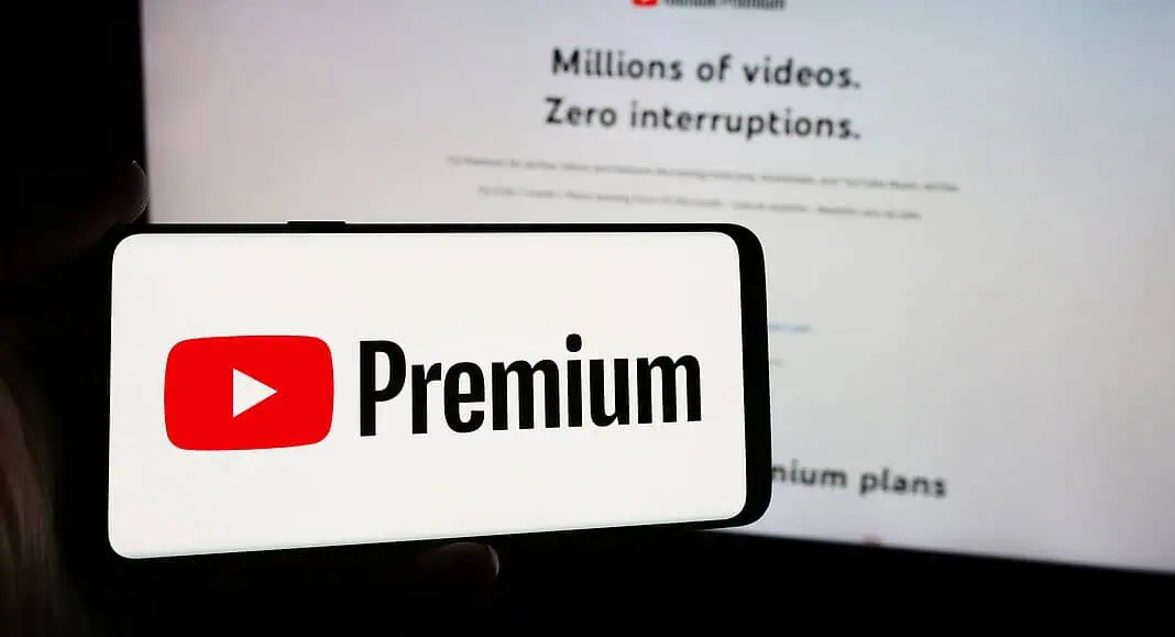 Un telefono mostra il logo di YouTube Premium davanti a una schermata che mostra il sito web di YouTube Premium, evidenziando funzioni come la condivisione con Piano Famiglia.
