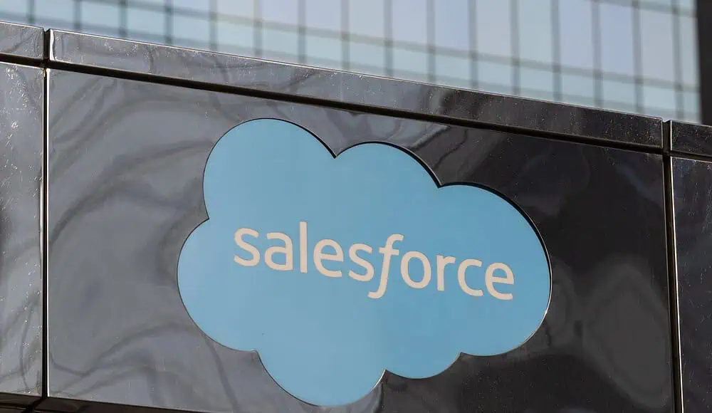 Un logo blu di Salesforce spicca sull'esterno riflettente di un edificio, con finestre di vetro sullo sfondo.