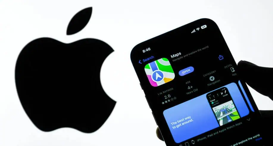 Una mano regge un telefono che visualizza la pagina dell'applicazione Apple Maps, con un grande logo Apple sullo sfondo, che evidenzia il design tipico di Apple.