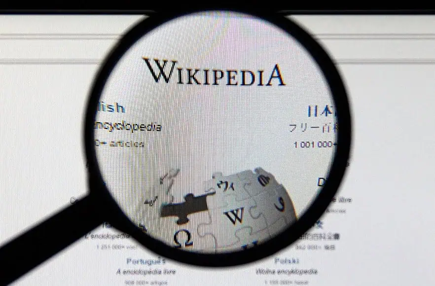 Una lente di ingrandimento si concentra sul logo di Wikipedia, evidenziando il simbolo iconico sullo schermo di un computer.