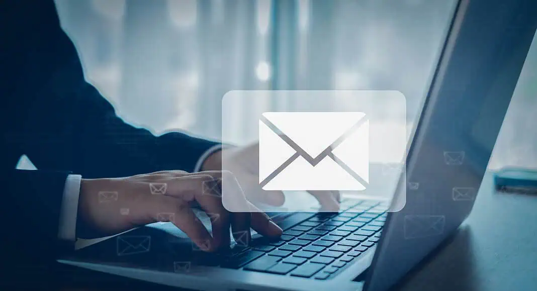 Persona che scrive su un computer portatile con l'icona di Gmail sovrapposta, a simboleggiare l'invio o la ricezione di e-mail.