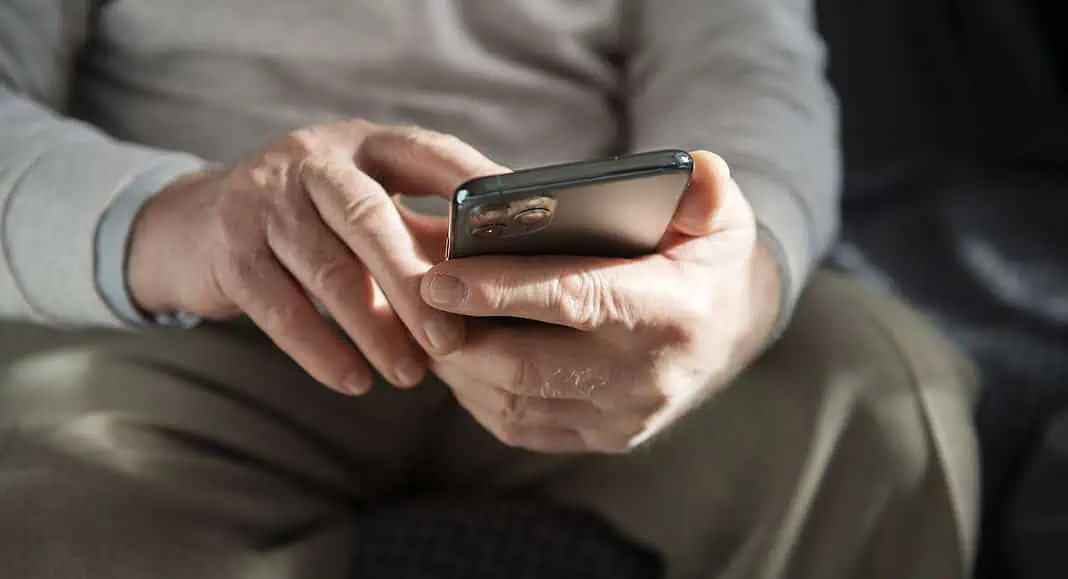 Primo piano delle mani di un anziano che tiene in mano e usa uno smartphone mentre è seduto e interagisce con le applicazioni Meta.