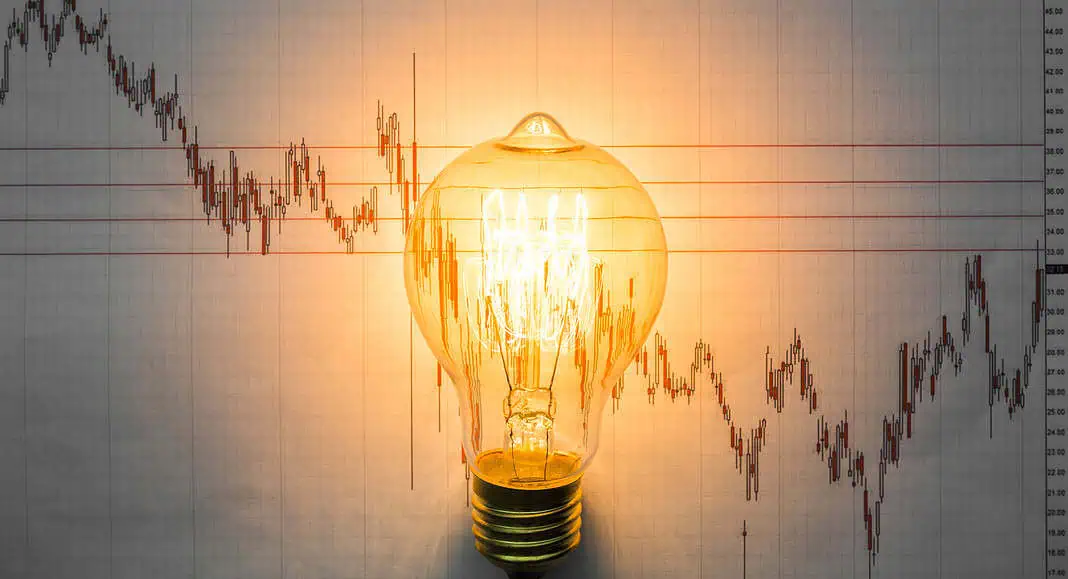Una lampadina incandescente davanti a un grafico di azioni finanziarie con linee fluttuanti, che simboleggia le intuizioni e l'innovazione guidate dall'intelligenza artificiale.