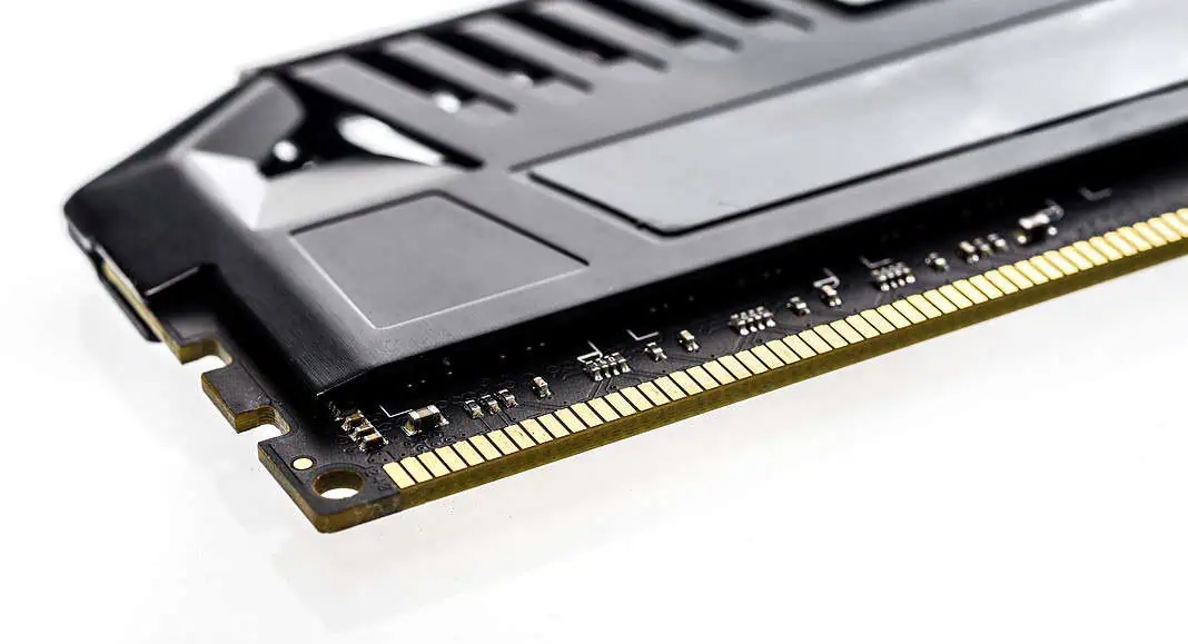 Primo piano di un modulo RAM memoria nero con pin di connessione dorati, visualizzato su uno sfondo bianco.