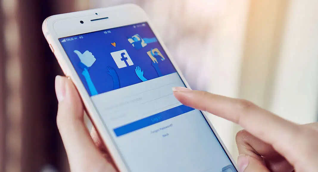 Una persona utilizza uno smartphone per accedere all'applicazione Facebook, toccando con un dito la schermata di login di Facebook.