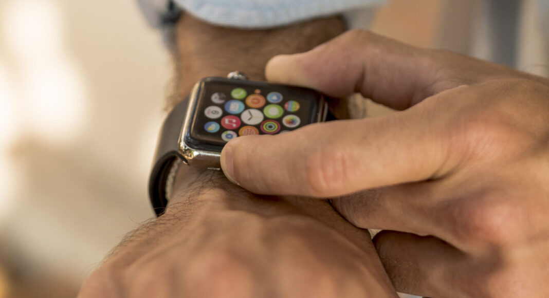 Persona che indossa uno smartwatch e ne tocca lo schermo, forse controllando una notifica di WhatsApp, vestita con una camicia azzurra e un top giallo chiaro.