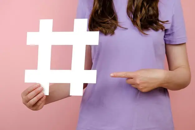 Donna con camicia viola che tiene in mano e indica un grande cartello hashtag bianco su sfondo rosa.